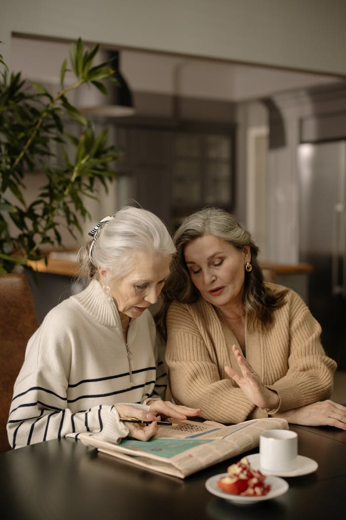 Two senior women enjoying a crossword puzzle together at a dining table in a cozy home setting.